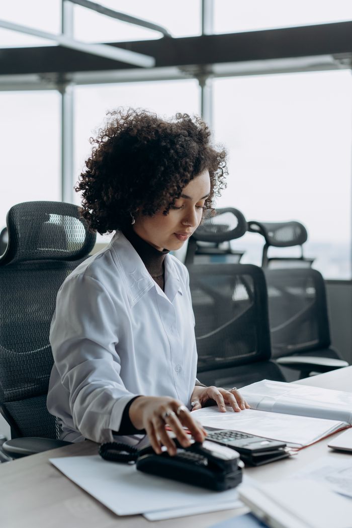 Young woman with curly hair working at a modern office desk, calculating numbers with focus.